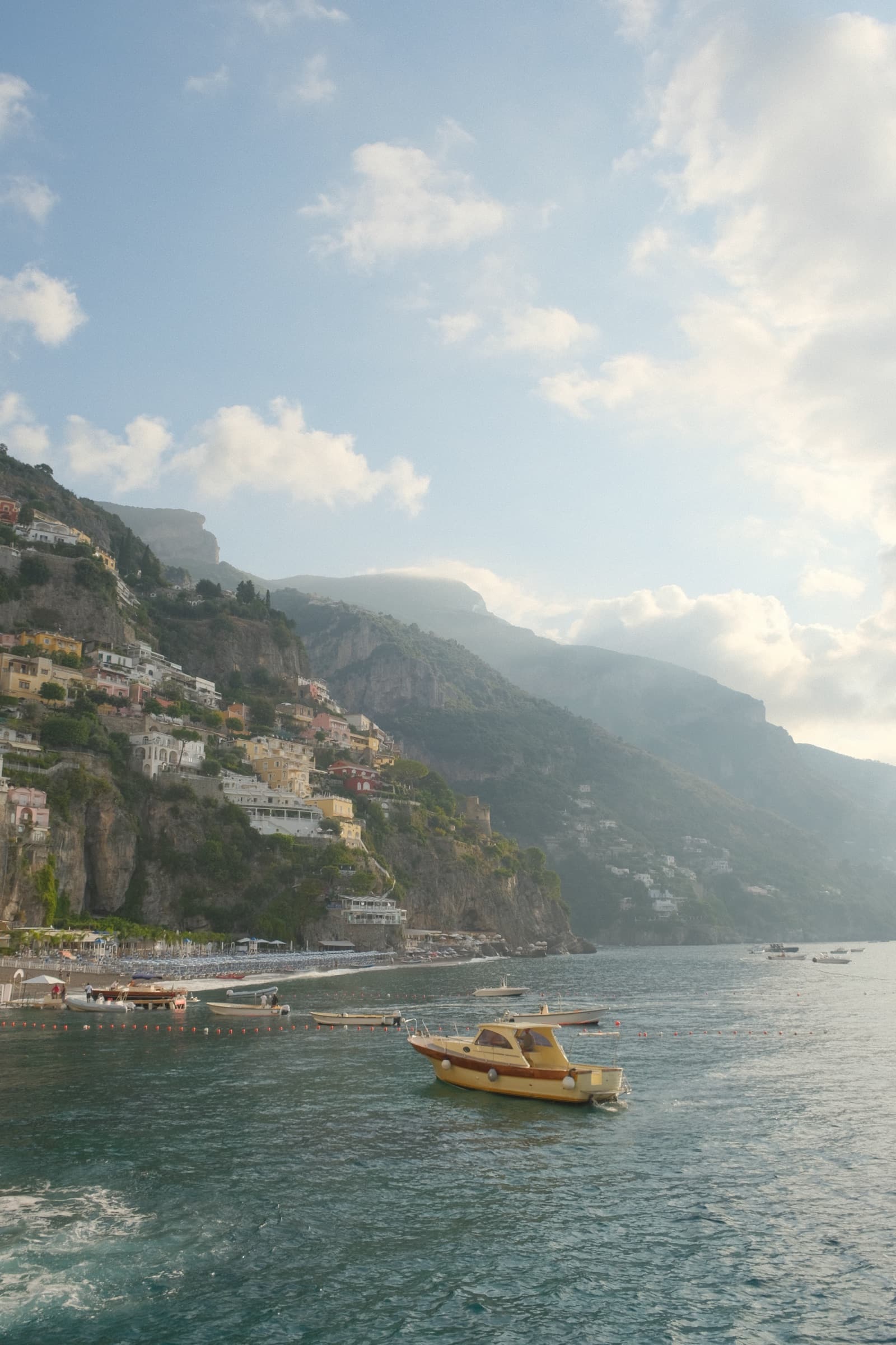 Boats on turquoise water beneath the stacked cliffside houses of Positano