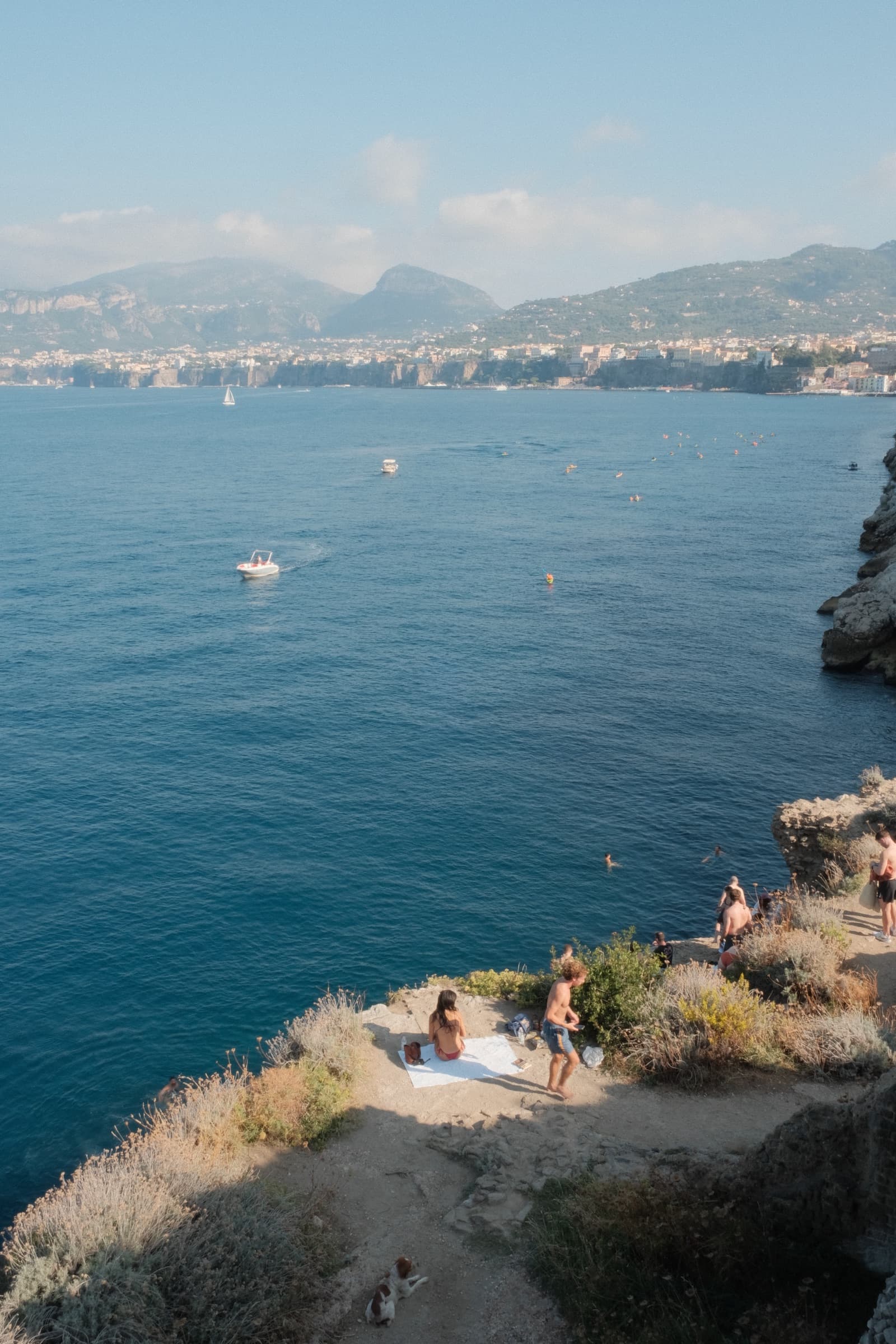 Swimmers and sunbathers on a rocky point above deep blue water in Sorrento