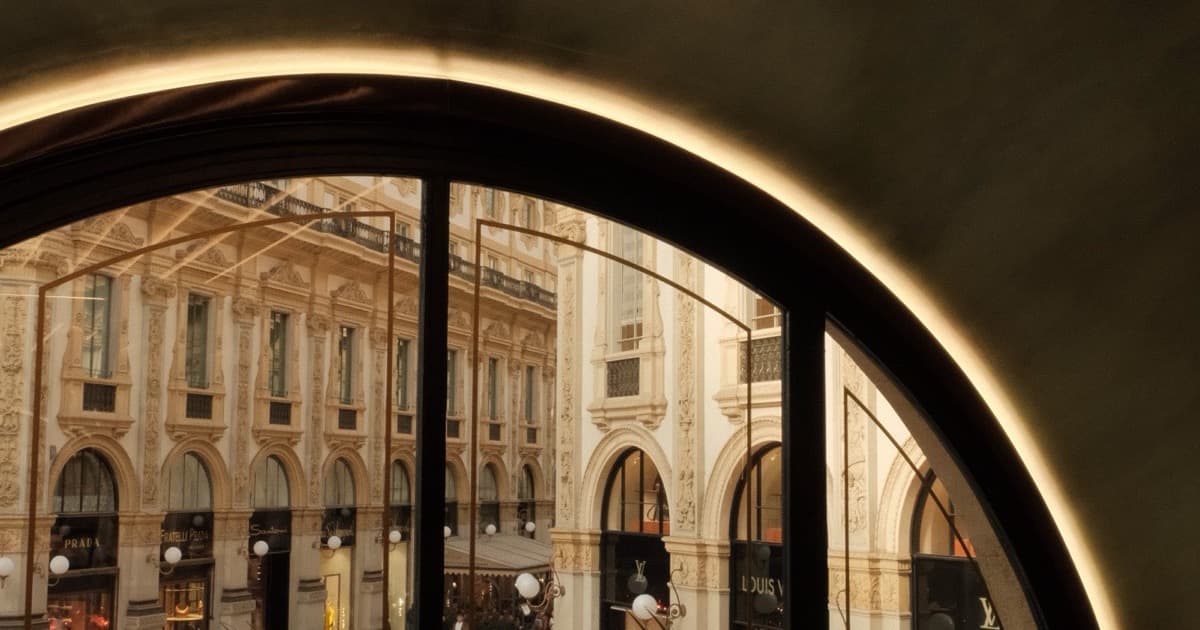 Warm light tracing a dark arch above a sunlit stone shopping arcade
