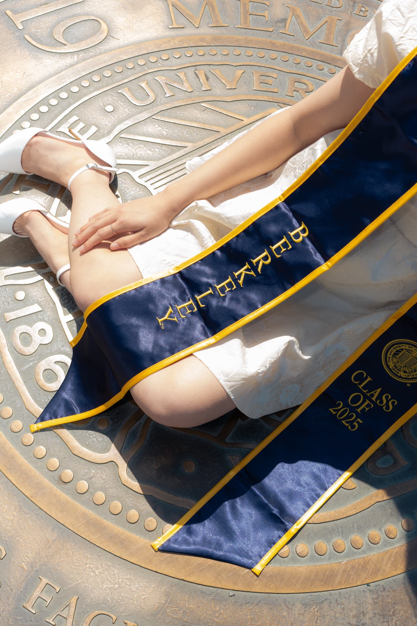 Detail of a Berkeley Class of 2025 stole and white heels resting on the bronze university seal
